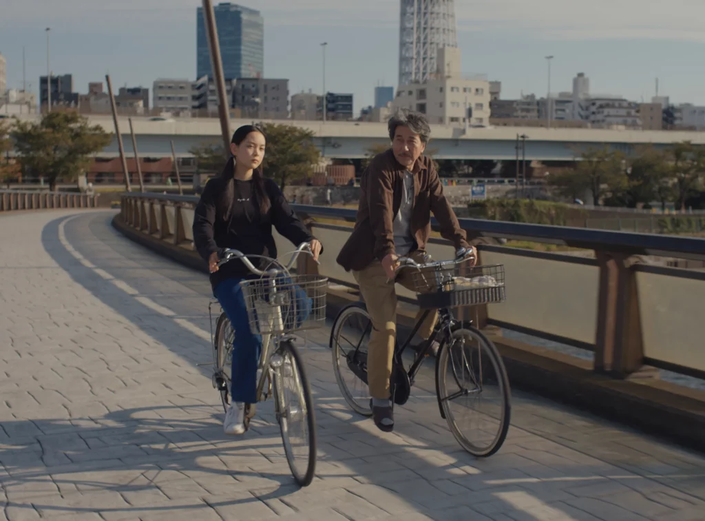 Perfect Days filminden iki karakterin bisikletlerine binip boş bir sokakta yolculuk etmesinin bir görüntüsü