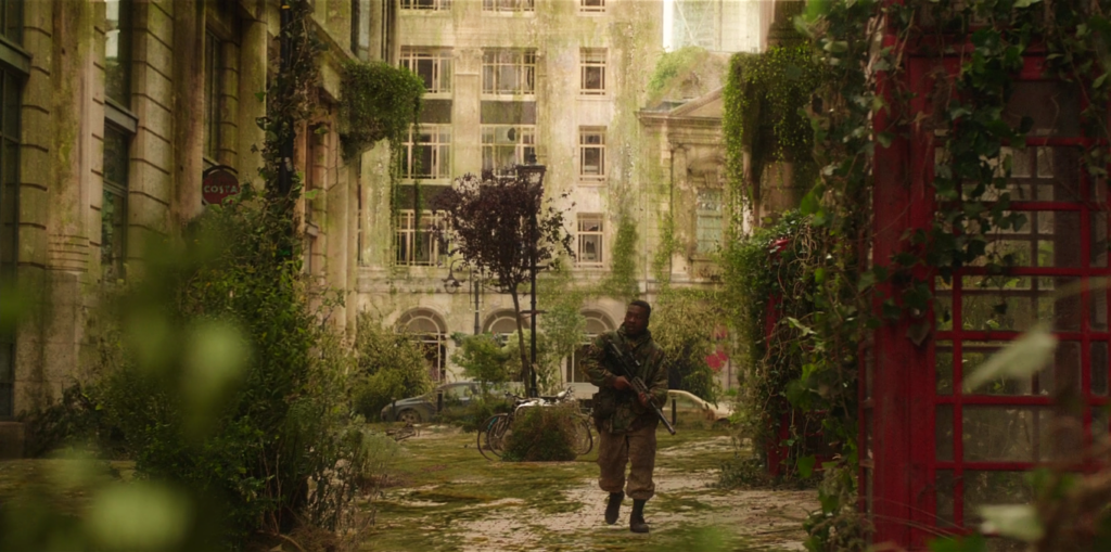 Tüm Sırların Sahibi Kız filminden bir görsel. Terk edilmiş bir şehrin sokaklarından birinde yürüyen bir asker. Etrafındaki binalar ve telefon kulübeleri, yapraklarla ve sarmaşıklarla çepeçevre sarılmış. 